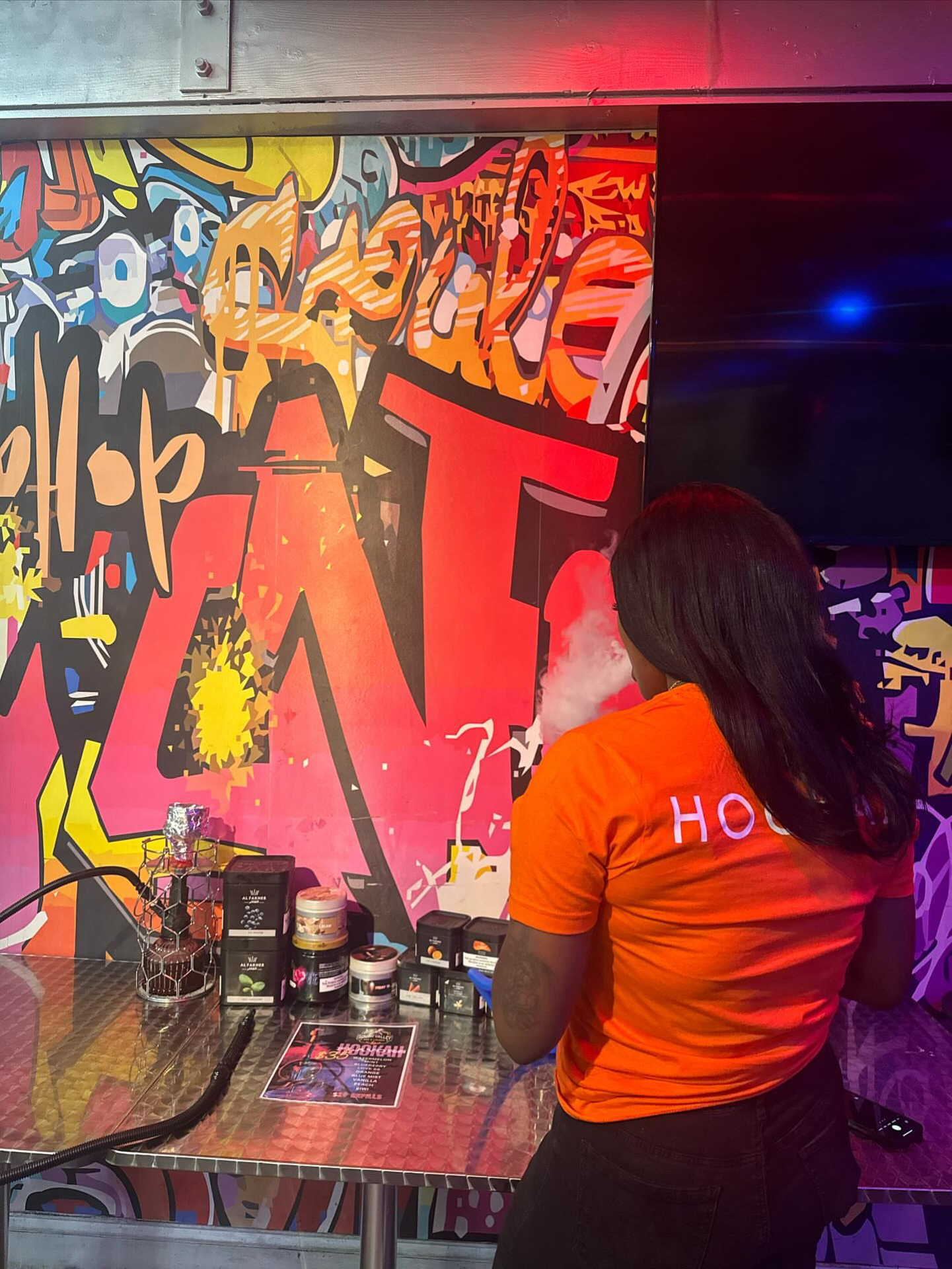 Heroes Hookah staff at the flavor bar with premium shisha jars and graffiti mural backdrop